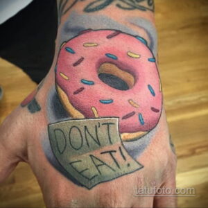 Фото тату розового пончика с посыпкой и надписью 'Don't Eat!' на костяшках пальцев.