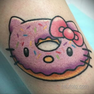 Фото тату с Hello Kitty, стилизованной под пончик. Розовый цвет, посыпка, бантик. Расположена на руке.