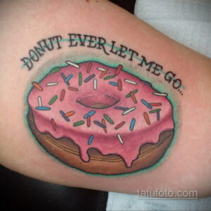 Фото тату розового пончика с разноцветной посыпкой и надписью "DONUT EVER LET ME GO" на руке. Оригинальный и забавный рисунок татуировки.