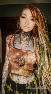 Фото татуировки на шее, груди и руках девушки с яркими цветами и мистическими символами. Татуировка выполнена в смешанном стиле.