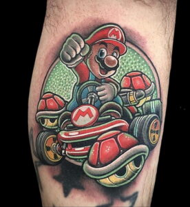Яркое фото тату с изображением Марио, гоняющего на карте в стиле Mario Kart на икре. Детализированный рисунок с использованием ярких цветов и динамичной композиции.