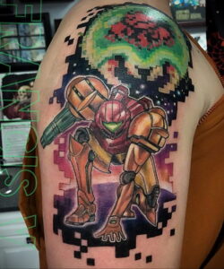 Яркое фото тату Самус Аран из Metroid в стиле пиксель-арт на плече. Детализированный рисунок с использованием ярких цветов и космического фона.