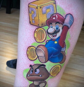Фото тату: Марио из Super Mario Bros., прыгает за монетами и вопросительным блоком, яркие цвета, на руке. Идеи для тату для поклонников Nintendo.