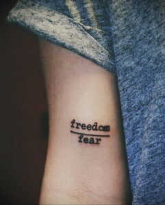 Фото татуировки на запястье с надписью 'freedom fear'. Черная надпись, выполненная простым шрифтом. Минималистичный рисунок татуировки.
