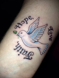 Фото тату голубя с надписями 'Hope', 'Faith', 'Love' на запястье. Нежный рисунок татуировки в стиле олдскул.