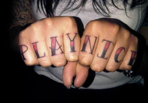 Фото тату: Надпись 'PLAYNITCH' на костяшках пальцев. Черно-красный рисунок татуировки, выполненный в стиле олдскул, с четкими контурами.