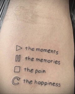 Фото татуировки на боку с изображением музыкальных символов (play, pause, stop) и слов 'the moments', 'the memories', 'the pain', 'the happiness'.