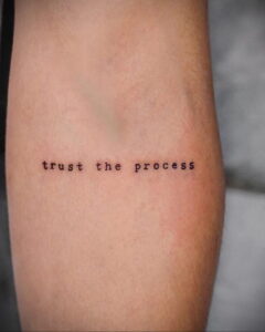 Фото тату с надписью 'trust the process' черным шрифтом на запястье. Минималистичный рисунок татуировки, простой эскиз для вдохновения.