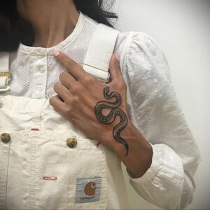 Фото тату: Черная татуировка змеи, обвивающей руку. Изящный рисунок с детальной проработкой чешуи.