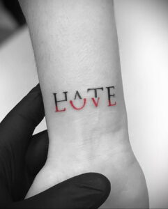 Фото тату с надписью 'HATE' и 'LOVE', выполненной в контрастных цветах на запястье. Символизирует двойственность человеческих эмоций и борьбу противоположностей.