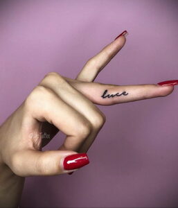 Фото татуировки с надписью 'luce' на пальце девушки. Минималистичный дизайн, черные чернила, аккуратный шрифт.