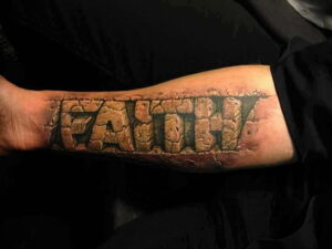 Фото тату на руке с надписью "FAITH", выполненной в виде высеченных в камне букв. Реалистичный рисунок татуировки.