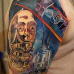 Фото тату с изображением C-3PO и R2-D2 из Звездных войн на плече. Детализированный рисунок в ярких цветах, выполненный опытным мастером.