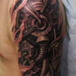 Фото тату: детализированная татуировка, имитирующая кибернетический протез, встроенный в руку, с металлическими деталями и проводами, на плече.