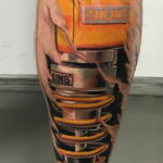 Фото тату: детализированная татуировка поршня двигателя с логотипом Ohlins, выполненная на голени в стиле биомеханики.