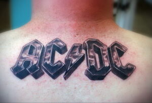 Фото татуировки с логотипом группы AC/DC на спине. Рисунок выполнен в черно-белой гамме с использованием теней.