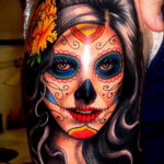 Фото тату: красочная татуировка в стиле сахарной черепушки (calavera) на плече. Детализированный рисунок с цветами и яркими узорами.