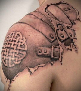 Фото тату в стиле blackwork, изображающего плечо в рыцарских доспехах с кельтским узором на наплечнике. Рисунок выполнен в черных тонах.