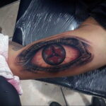 Фото тату: глаз с символом Sharingan из аниме Naruto. Детализированный рисунок с красными трещинами и ярким символом.