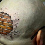 Фото тату: иллюзия кирпичной стены, пробивающей лысую голову. Реалистичный 3D рисунок с использованием коричневых и серых оттенков.