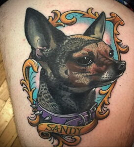 Цветное тату чихуахуа в стиле олдскул на бедре, с подписью 'Sandy' на ленте. Детализированный рисунок с яркими цветами и четкими контурами.