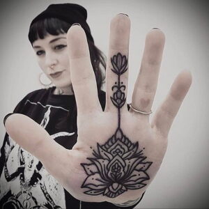 Фото тату: сложный узор в виде цветка лотоса, выполненный в технике blackwork на ладони девушки. Детализированный рисунок с геометрическими элементами.