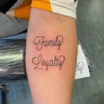 Фото тату на руке с надписью 'Family Loyalty' выполненной каллиграфическим шрифтом. Простая и лаконичная татуировка, символизирующая ценность семьи.