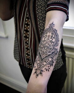 Фото татуировки на предплечье в стиле хенд-поук (henna-inspired), выполненной в черном цвете с изящными узорами и растительными элементами.