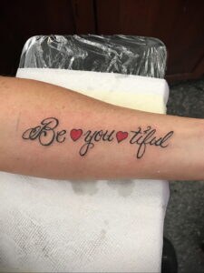 Фото татуировки надписи "Be you-tiful" с сердечками на предплечье. Милая и вдохновляющая тату для тех, кто ценит позитив и самовыражение.