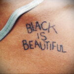 Фото тату на груди с надписью "Black is Beautiful", выполненной простым шрифтом. Черно-белый рисунок, символизирующий гордость и самоидентификацию.