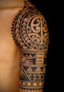 Фото тату: традиционный полинезийский узор, покрывающий плечо и часть груди. Черные геометрические элементы и символы.