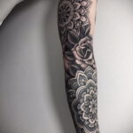 Фото тату: черно-белая татуировка на руке с изображением мандалы и розы. Сложные узоры и детализированная проработка создают впечатляющий рисунок.