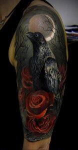 Фото тату на руке: черный ворон, сидящий среди красных роз на фоне луны и деревьев. Мистический и загадочный рисунок.