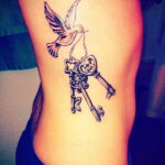 Фото тату ключей и летящего голубя на боку. Черно-белый рисунок с детальной проработкой элементов.
