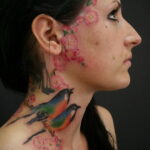 Фото тату двух птиц на фоне цветущей сакуры, выполненное в акварельном стиле на шее и плече девушки.