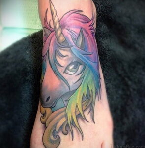 Фото тату: красочная татуировка головы единорога с радужной гривой на предплечье. Реалистичный стиль, яркие цвета.