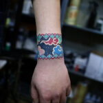 Фото тату на запястье: красочный браслет с геометрическими узорами и облаками, выполненный в этническом стиле.