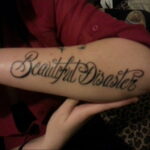 Фото тату надпись "Beautiful Disaster" на предплечье. Черно-белый рисунок татуировки выполнен каллиграфическим шрифтом.
