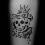 Фотография татуировки на руке, изображающей череп в короне с надписью 'Memento Mori'. Татуировка выполнена в стиле традиционной татуировки.