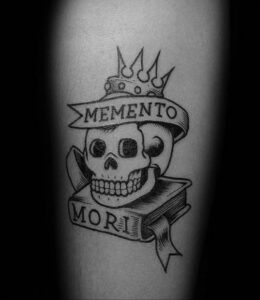 Фотография татуировки на руке, изображающей череп в короне с надписью 'Memento Mori'. Татуировка выполнена в стиле традиционной татуировки.