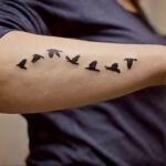 Фотография мужской руки с минималистичными татуировками птиц, летящих в ряд.