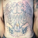 Фото тату двуглавого орла на животе. Черно-белый рисунок татуировки с детально проработанными перьями и мощной композицией.