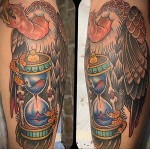 Фото татуировки в стиле олдскул с изображением орла над песочными часами. Яркие цвета, четкие контуры и традиционные элементы.