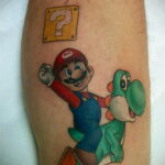 Фото тату на руке, изображающее Марио и Йоши из игры Super Mario Bros. Классический стиль и яркие цвета.