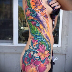 Фото тату: Яркая и красочная татуировка с изображением тропических цветов и листьев на боку. Детализированный рисунок татуировки в ярких цветах.