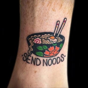 Фото татуировки на запястье: миска с лапшой и палочками, надпись "Send Noods" в традиционном стиле.