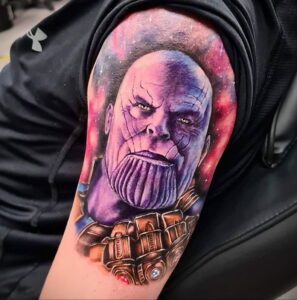 Фото татуировки на плече с изображением Таноса из вселенной Marvel. Яркий и детализированный рисунок татуировки с использованием различных цветов.