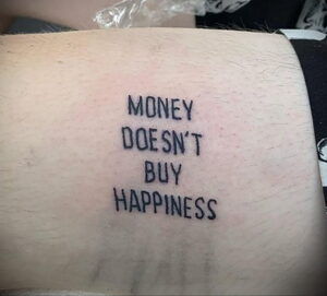 Фото минималистичной татуировки с надписью 'Money Doesn't Buy Happiness' (Деньги не покупают счастье), выполненной простым шрифтом.