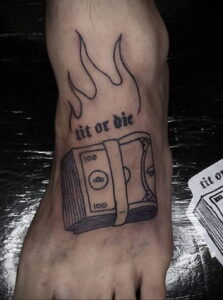 Фото тату на стопе, изображающее надпись 'Lit or Die' и пачку денег, охваченную пламенем, выполненное в минималистичном стиле.