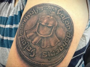 Фото тату с изображением монеты, выполненной в технике blackwork, на плече. Черно-белый рисунок татуировки.